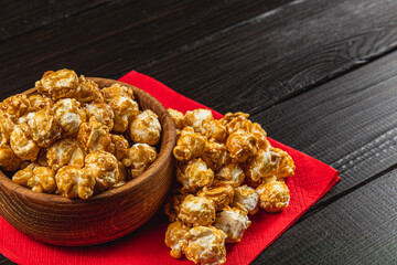 Snack, movie concept, caramelized popcorn in a wooden bowl on a red napkin
