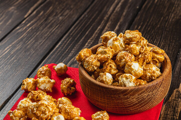 Snack, movie concept, caramelized popcorn in a wooden bowl on a red napkin