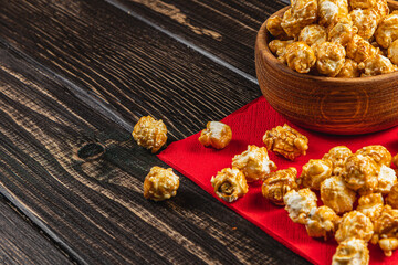 Caramelized popcorn in a wooden bowl on a red napkin on a wooden table