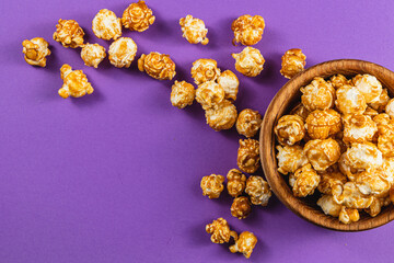 Sweet caramelized popcorn in a wooden bowl on a purple background, top view