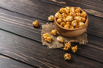 Snack, movie concept, caramelized popcorn in a wooden bowl on a wooden table
