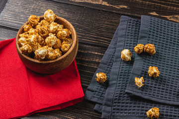 Snack, movie concept, caramelized popcorn in a wooden bowl on a red napkin