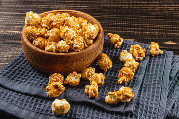 Snack, movie concept, caramelized popcorn in a wooden bowl on a wooden table