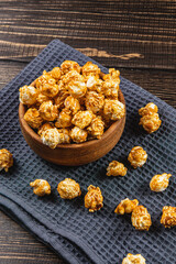 Snack concept, caramelized popcorn in a wooden bowl on a gray, wooden background