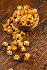 Snack, movie concept, caramelized popcorn in a wooden bowl on a wooden table