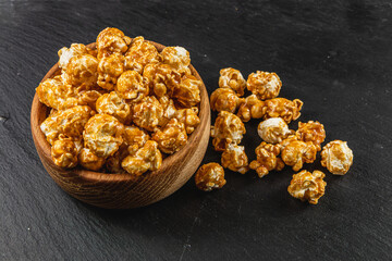 Snack concept, sweet caramelized popcorn in a wooden bowl on a black background