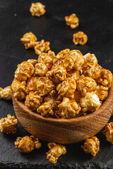 Snack concept, sweet caramelized popcorn in a wooden bowl on a black background