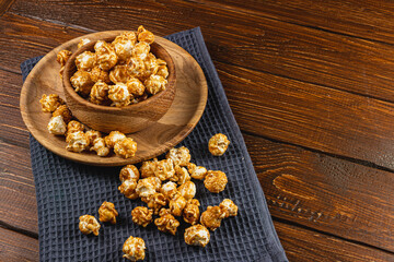 Caramelized popcorn in a wooden bowl with a plate on a wooden background