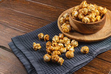 Caramelized popcorn in a wooden bowl with a plate on a wooden background