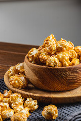 Caramelized popcorn in a wooden bowl with a plate on a wooden background