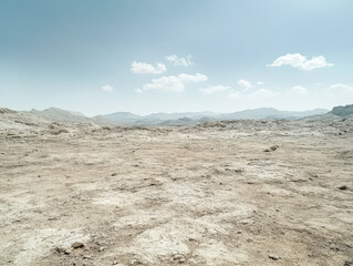 Vast barren landscape with dry terrain and soft clouds under bright sky