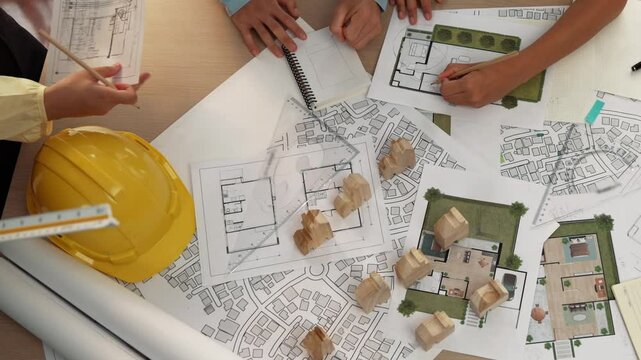 Architect and safety engineer discussion about building construction use blueprint on table with architectural document, measurement tool and wooden block scatter around at modern office. Delineation.