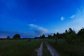 Fototapeta premium A tranquil night scene featuring a mist-covered field illuminated by the starry sky. The vibrant blue hues of the night sky and scattered clouds create a serene and mystical atmosphere. 