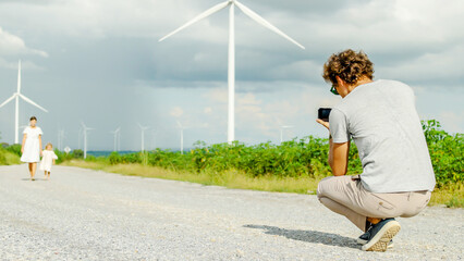 A joyful girl runs through a picturesque landscape with wind turbines in the background, Child is running towards her father who is welcoming her with open arms, environment and bonding of family.