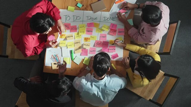 Top view of people writing and making scrum task board while writing marketing and planning strategy at colorful sticky notes. Smart team manage work performance by using kanaban board. Convocation.
