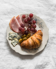 Homemade breakfast - a plate with croissant, ham, cheese, grapes and olives on the  light background
