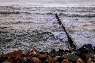 Fototapeta premium Calm Ocean Waves Gently Lap Against a Rocky Jetty at Dawn Near a Serene Coastline