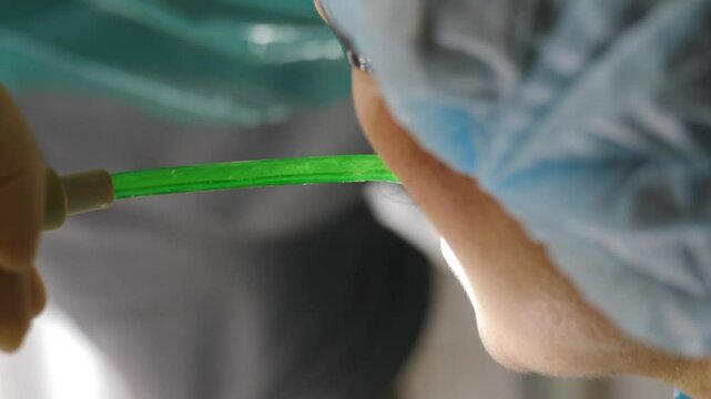 Close up view of a dentist conducting a dental procedure. Vertical footage. The dentist uses a saliva ejector and dental drill while prioritizing patient comfort and maintaining a sterile environment