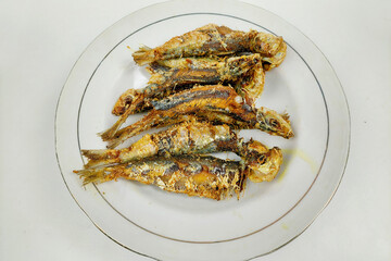 Small fried fish on a white plate on the dining table