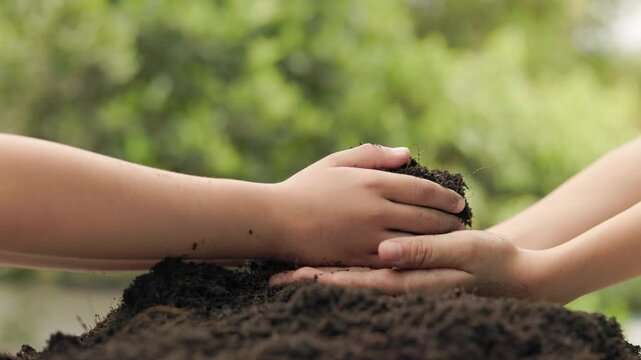 in a gentle act of love, the younger sibling pours dark fertile soil into the waiting hands of the elder, reflecting hope, care and the promise of nurturing the earth together, green garden background