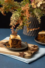 Iced carrot cake sllice served on grey pewter plate with chocolate star and mid blue table cloth, luxury earthy feel