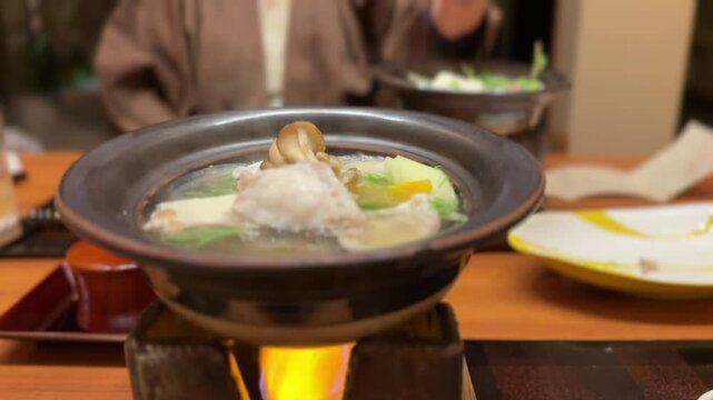 冬の味覚　トラフグのてっちり鍋のコンロと向かいの女性が鍋の蓋を取るシーン
