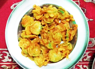 A plate filled with crispy, deep-fried snacks, possibly vegetable fritters, sits on a patterned red tablecloth. The golden-brown pieces appear freshly cooked and ready to be enjoyed.