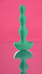 Green anal beads on pink mirror background. 