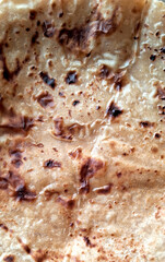 A close-up view of a flatbread showcases its crispy texture and browned spots, indicating it has been perfectly toasted. The golden-brown hues and uneven surface add to the rustic charm of the bread.