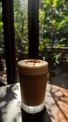 A glass of coffee topped with froth, set against a lush green background.