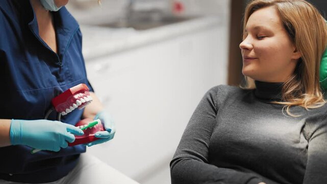 Woman talking with dentist about hygiene of oral cavity for save teeth health. Doctor showing how to clean teeth by toothbrush in modern dental clinic, stay healthy and beautiful, portrait of client