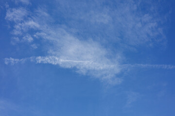 Clouds resembling delicate brush strokes drift across a clear blue sky, creating a serene and...