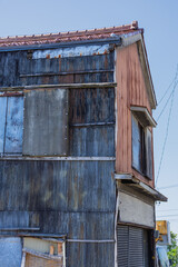 A weathered building showcases corrugated metal siding and a small, protruding window. The mix of distressed materials and natural colors adds an abandoned, rustic charm under a clear sky.