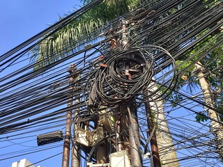 Low angle shoot of messy tangled cable electrical wire on utility pole against a blue sky .