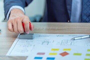 A person in a suit stamping a document with a red stamper.