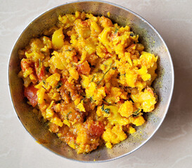 A bowl is filled with a vibrant, homemade potato dish, featuring yellow & orange tones with visible herbs & spices. The food appears freshly cooked, showcasing an appetizing blend of textures & colors