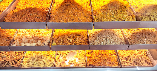 A variety of Indian snacks are neatly arranged in a display case, each section filled with different types of fried and savory treats.