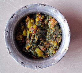 A metal bowl is filled with a vibrant, colorful dish featuring chunks of vegetables and leafy...