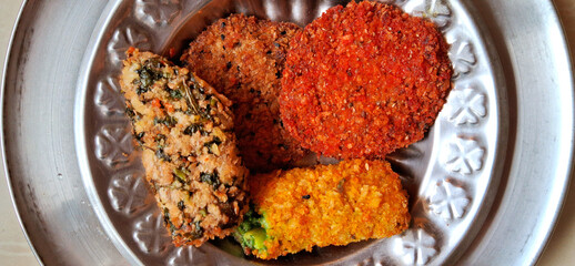 A metal plate holds an assortment of colorful breaded and fried snacks, including circular and oval shapes with varying shades of red, orange, and brown. 