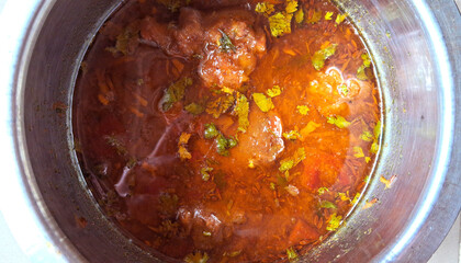 A pot contains a richly seasoned tomato-based curry, garnished with fresh cilantro leaves. Warm hues and visible spices suggest a flavorful and aromatic dish.