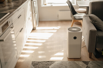 White air purifier from dust and viruses in the interior of the apartment opposite the sofa with sun rays. Health and technology.