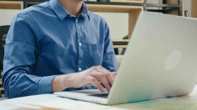 A close up, no face shot of hands of a corporate office male employee or employee in formal attire using and typing on a laptop, working on an assignment in a modern start up business workplace.