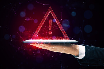 Warning sign hologram hovering above a tablet held by a hand on a dark background.