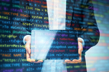 Businessman holding transparent tablet with programming code overlay on a digital background.