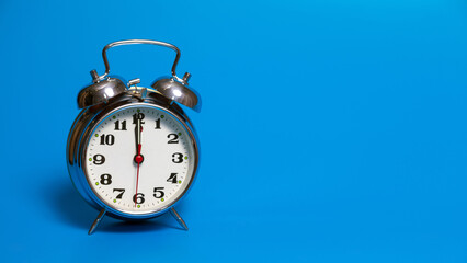 Vintage alarm clock on blue background showing midnight, noon. Retro clock close-up. Classic analog alarm clock in old style with copy spice.