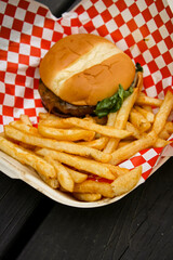 American style cheeseburger on a paper box with french fries. The background is a wooden balcony.