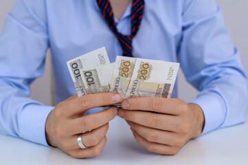 Mężczyzna trzyma w dloni polskie banknoty pln, ma długi, problemy finansowe