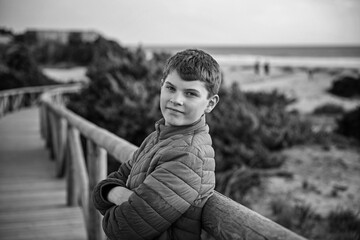 Happy cheerful teenager standing on beach at sunset. happy preteen handsome boy smiling at the camera. Kid on family vacation at the sea.