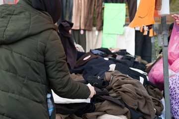 People looking at a pile of second hand clothes in a flea market.