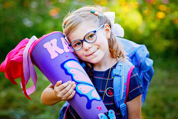 Happy little kid girl with eye glasses with backpack or satchel and big school bag or gift cone...